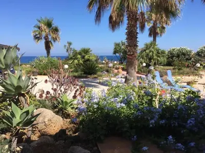 a garden with flowers and palm trees and the ocean at Apartment Villa Gina in Trappeto by Interhome in Trappeto