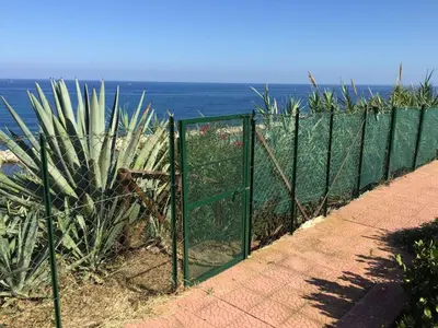 a green fence next to the ocean with a plant at Apartment Villa Gina in Trappeto by Interhome in Trappeto