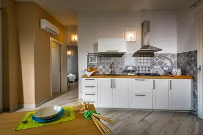 a kitchen with white cabinets and a wooden floor at APT RINO Sea View basement in Villa Rosaria in Scopello