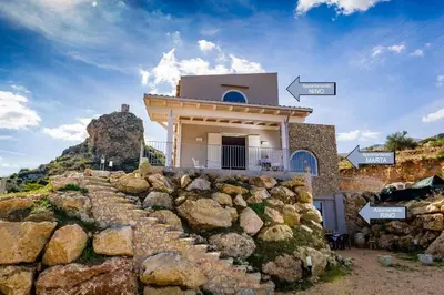 a house on top of a mountain with a rock wall at APT RINO Sea View basement in Villa Rosaria in Scopello