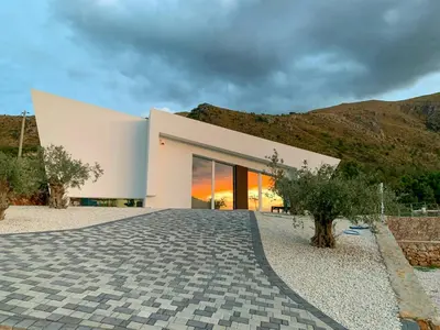 a large white building with a hill in the background at Sustainable Villa With Infinity Pool in Castellammare del Golfo