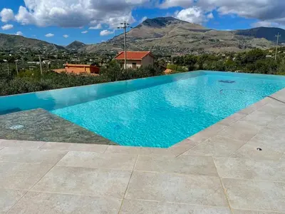 a blue swimming pool with mountains in the background at Sustainable Villa With Infinity Pool in Castellammare del Golfo