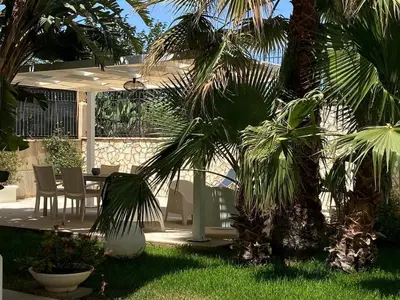 a patio with a table and chairs and palm trees at Nereide home 350 sqm with large garden in Balestrate