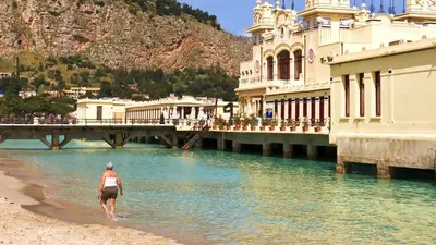 a woman walking on the beach next to a bridge at Aurora Home Suite in Palermo