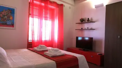 a bedroom with a bed with red curtains and a tv at Apartment Papyri in Palermo