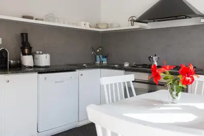 a kitchen with white cabinets and a white table with red flowers at White and Sea Villa fronte mare a Mondello Addaura in Palermo
