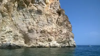 a rocky cliff with a boat in the water at Casa Vacanze La Terrazza Sul Golfo in Castellammare del Golfo