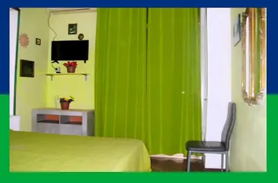 a green wall in a bedroom with a chair and a television at Santa Oliva Homestay in Palermo