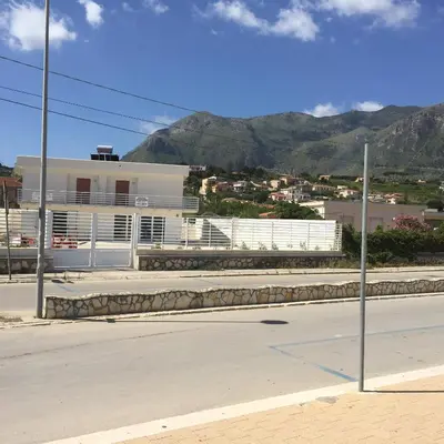 a street with a white building with mountains in the background at Casa Vacanze Playa 54 in Castellammare del Golfo