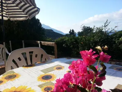 a table with flowers and two chairs and an umbrella at Two Steps From The Sea in Scopello