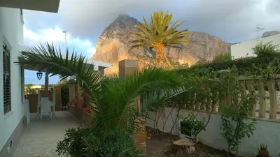 a building with palm trees and a mountain in the background at B&B Villa Bea in San Vito lo Capo