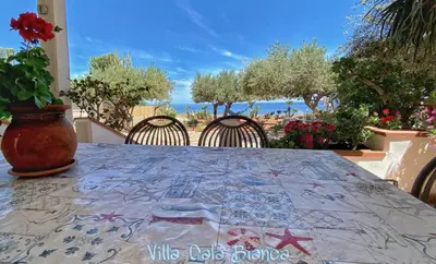 a table with chairs and a table with a view of the ocean at Villa Cala Bianca in Castellammare del Golfo