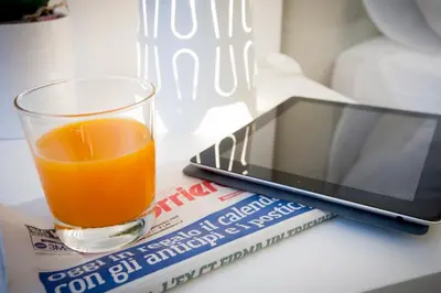a glass of orange juice next to a book and a tablet at Politeama Apartments by Giorgio in Palermo