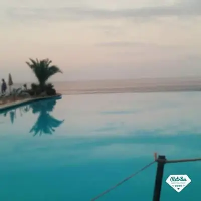 a swimming pool with a palm tree and the ocean at Vicino al mare e lontano dai rumori in Alcamo Marina