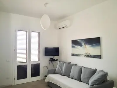 a white living room with a couch and a tv at Un mare di Blu - Casa Cobalto in Macari