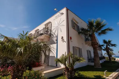 a white building with a palm tree in front of it at Marina di Petrolo Hotel & SPA in Castellammare del Golfo