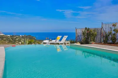 a swimming pool with two lounge chairs and the ocean at Villa Tarì in Scopello