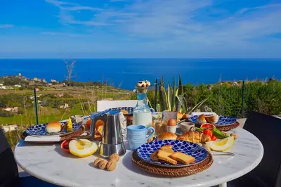 a table with a plate of food and a bottle of wine at Villa Tarì in Scopello