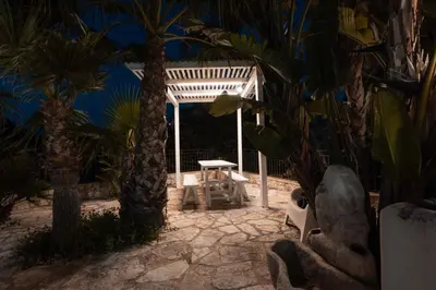 a patio with a white pergola with palm trees at Villa Oleandro in Alcamo Marina