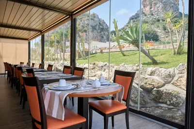 a dining room with tables and chairs and a large window at Baglio Dello Zingaro in Scopello