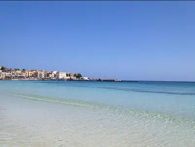 a beach with blue water and buildings in the background at Villa Pinella in Palermo