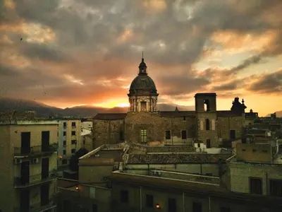 an old building with a clock tower with a sunset in the background at Casa pergj in Palermo