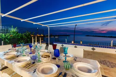 a table with plates and bowls on it with a view of the ocean at Vero Sicily - Villa San Giorgio in Cinisi