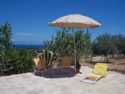three chairs and an umbrella on a patio at Antico Rustico in Scopello