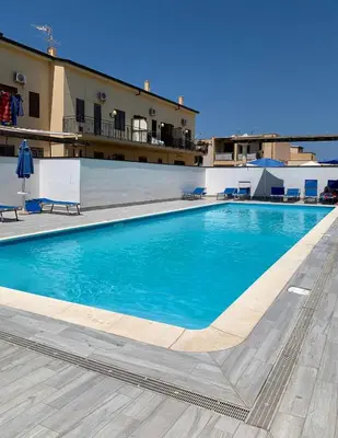 a large blue swimming pool in front of a building at Coral sea in San Vito lo Capo