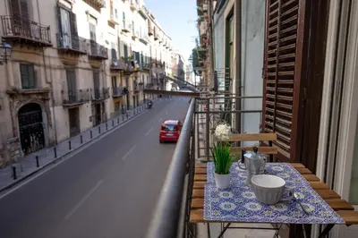 a table on a balcony with a red car on a street at Loft Piazza Marina Family by DomuSicily in Palermo