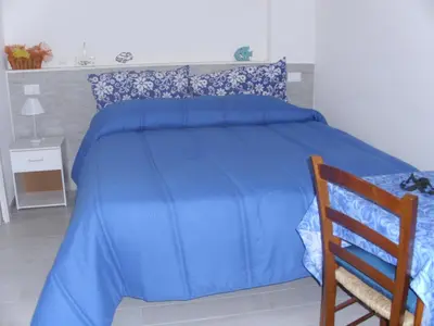 a blue bed with a blue comforter and a wooden chair at Casa di Cecilia in Castellammare del Golfo