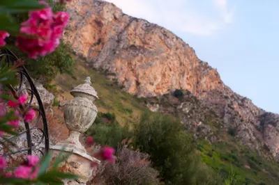 a stone vase sitting next to a mountain with pink flowers at Cala Dell'Arena in Macari