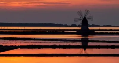 a windmill in the water with a sunset in the background at Villa Hibiscus Scopello in Scopello