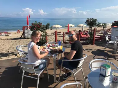 a man and woman sitting at a table on the beach at Villa Pasquale...immersa nella tranquillita' in Lascari
