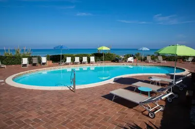 a swimming pool with chairs and an umbrella at Riva Sea Apartments in Castellammare del Golfo