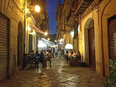 a city street at night with people sitting at tables at Orologio del Massimo in Palermo