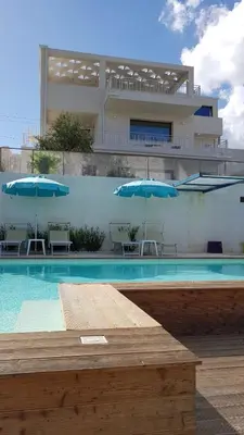 a swimming pool with blue umbrellas and a building at Villa Vo' Scurá in Alcamo Marina