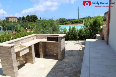 a stone barbecue grill on a patio next to a pool at Borgo Aranci - Appartamento in Villa Garofalo - 15B in Castellammare del Golfo