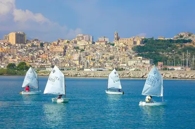 four small sailboats in the water with a city in the background at La Casetta di Andrea & Vale in Termini Imerese