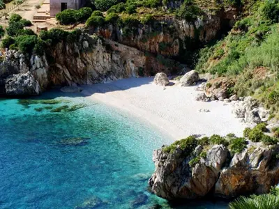 a beach with blue water and rocky cliffs at Il Sole di Sicilia in Castellammare del Golfo