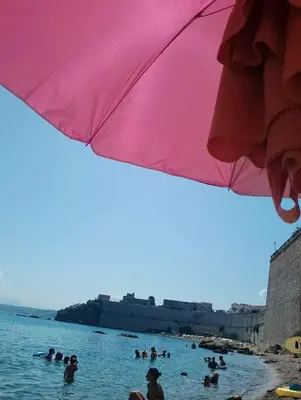 a group of people in the water under a pink umbrella at Marina in Castellammare del Golfo