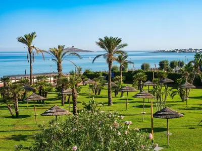 a lawn with umbrellas and palm trees and the ocean at Saracen Sands Hotel & Congress Centre - Palermo in Isola delle Femmine