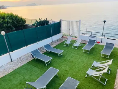 a group of chairs and tables on a lawn with the ocean at Sfondo Blu Villa sul mare in Trabia