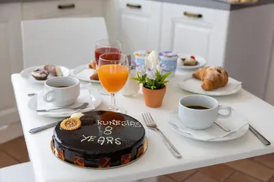 a table with a cake and cups of coffee and croissants at Kunesias B&B in Cinisi