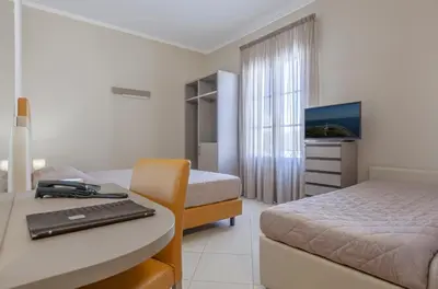 a room with two beds and a desk with a laptop at Ghibli Hotel in San Vito lo Capo