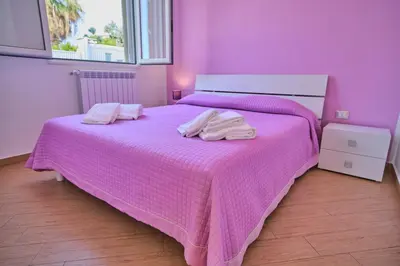 a pink bedroom with a bed with two towels on it at Villa Sicilia in Lascari