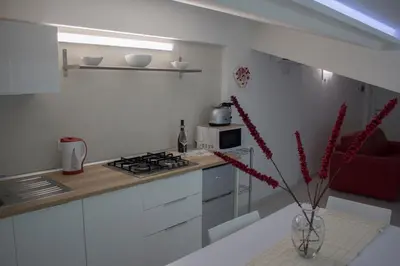 a white kitchen with a vase with red flowers in it at Duchessa House in Castellammare del Golfo