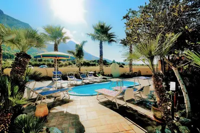 a swimming pool with chairs and palm trees in a resort at Villa Minoa con piscina in San Vito lo Capo
