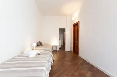 two beds in a room with white walls and wooden floors at GuestHost - Quattro Canti Charming Flat in Palermo
