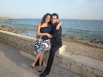 a man and a woman sitting on a wall by the ocean at Sunrise in Lascari